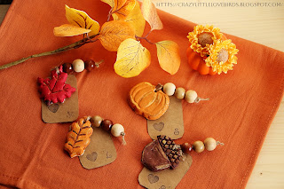 Completed clay place cards displayed on an orange Kitchen hand towel near yellow faux leaves and yellow daisies inside of a mini orange pumpkin vase